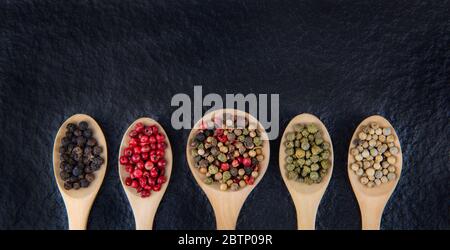 Plat de 5 types de grains de poivre dans une cuillère en bois sur fond noir concept alimentaire sain Banque D'Images