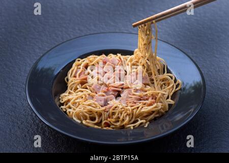 Spaghetti au jambon mélangé Spicy sur une assiette noire Banque D'Images