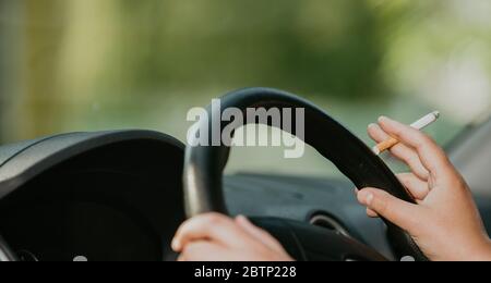 Jeune femme fume une cigarette tout en conduisant une voiture, concept de transport Banque D'Images