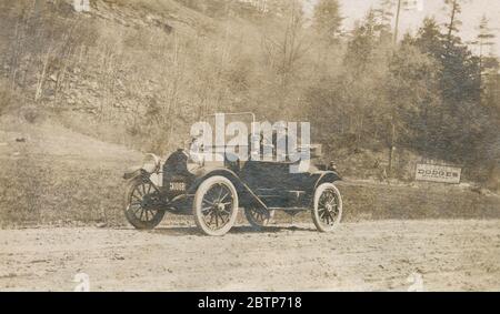 Photographie antique d’avril 1913, New Hampshire homme « sur la route de Windsor » dans son automobile Detroiter avec le signe pour Dodge’s Pharmacy en arrière-plan. Le Detroiter a été réalisé par la Briggs-Detroiter Company de Detroit, Michigan. SOURCE : PHOTO ORIGINALE Banque D'Images