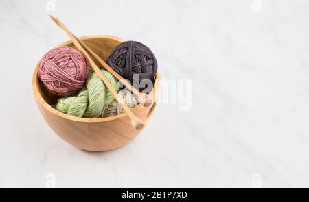Bol à tricoter rempli de balles de fil coloré avec aiguilles à tricoter en bois sur fond neutre Banque D'Images