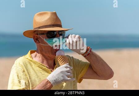 Southsea, Portsmouth, Angleterre du Sud, Royaume-Uni. Mai 2020. Homme mangeant de la glace tout en portant un masque et des gants de protection en caoutchouc pendant le Corvid-19 dehors Banque D'Images