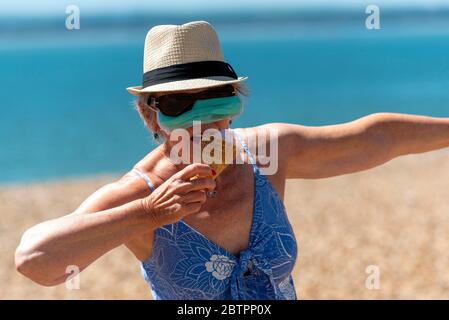 Southsea, Portsmouth, Angleterre du Sud, Royaume-Uni. Mai 2020. Femme mangeant de la crème glacée tout en portant un masque pendant l'épidémie de Corvid-19. Banque D'Images