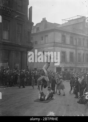 Le théâtre est le pavé. Des acrobates au bord du trottoir, offrant un divertissement supplémentaire pour la foule de personnes qui attendent d'entrer dans le Lyceum Theatre, Londres, pour voir le pantomime « Beauté et la Bête » le lendemain de Noël, le jour férié, qui suit le jour de Noël. Les artistes de la rue, notamment les chanteurs, les danseurs et les comédiens, sont un élément bien établi de la vie théâtrale de Londres. Comme les places moins chères dans la fosse et la galerie du théâtre de Londres ne peuvent pas être réservées, de longues files d'attente de personnes attendaient dehors pour s'assurer des meilleures places quand le théâtre ouvre ses portes. Les longues heures d'attente Banque D'Images