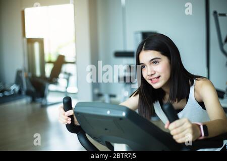 Mettre en forme la jeune fille en utilisant le vélo d'exercice à la salle de gym. Une femme de fitness utilise un vélo d'air à la salle de gym. Banque D'Images