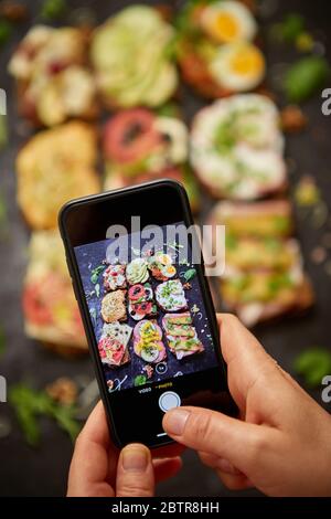 Femme faisant une photo avec un smartphone d'assortiment de sandwichs maison avec différentes garnitures Banque D'Images