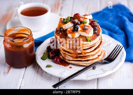 Délicieux petit déjeuner sur une table légère. Crêpes sur une assiette bleue avec banane et caramel salé Banque D'Images