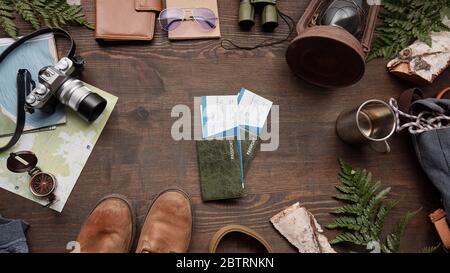 Vue au-dessus des passeports étrangers et billets d'avion sur une table en bois avec brindilles, bottes, thermos mug et appareil photo, plat Banque D'Images