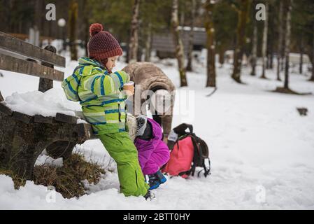 Mère avec deux enfants à l'extérieur dans un paysage enneigé se reposant pendant une promenade et une exploration. Banque D'Images