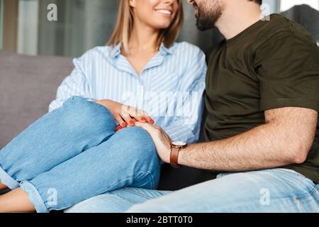 Photo rognée d'un couple caucasien gai souriant et enembrassant tout en étant assis sur un canapé à la maison Banque D'Images