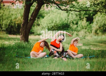 L'entraîneur aide les enfants à terminer l'exercice. Faites du sport en plein air. Concept de mode de vie sain. Yoga pour bébé, entraînement physique. Banque D'Images