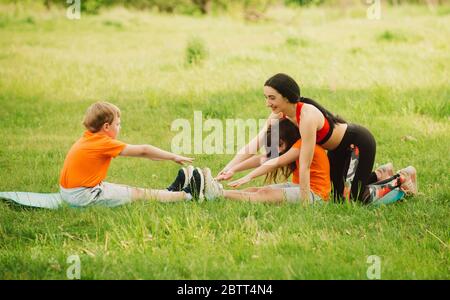 La mère aide les enfants à terminer l'exercice. Faites du sport en plein air. Concept de mode de vie sain. Yoga pour bébé, entraînement physique. Banque D'Images