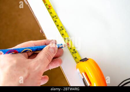 Un homme mesure le papier peint à la longueur à l'aide d'un mètre-ruban rétractable en métal et d'un crayon. Banque D'Images