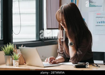 Femme d'affaires utilisant un ordinateur portable et une calculatrice pour faire des finances mathématiques sur un bureau en bois dans le bureau Banque D'Images