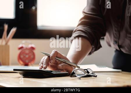 Femme d'affaires utilisant une calculatrice pour faire des finances mathématiques sur un bureau en bois dans le bureau et les affaires de travail, Banque D'Images