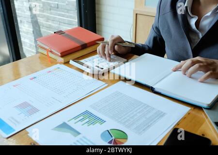 Femme d'affaires utilisant une calculatrice pour faire des finances mathématiques sur un bureau en bois dans le bureau et les affaires de travail, Banque D'Images