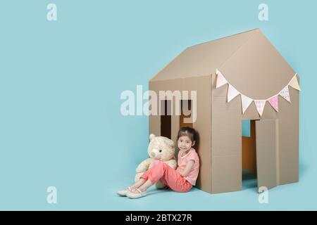 Petite fille asiatique jouant avec la maison en carton avec son ours en peluche isolé sur la bannière longue bleue avec l'espace de copie pour votre texte, Creative à la maison Banque D'Images