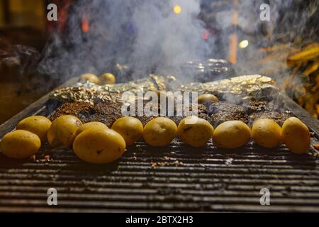 Brochettes de pommes de terre et poisson grillés dans du papier aluminium avec fumée du gril. Fête barbecue. Banque D'Images