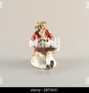Figure d'un mendiant jouant le HurdyGurdy. Recherche en ProgressSmiling musicien portant des vêtements déchirés, assis sur un affleurement blanc, jouant un hurdy-gurdy. Banque D'Images