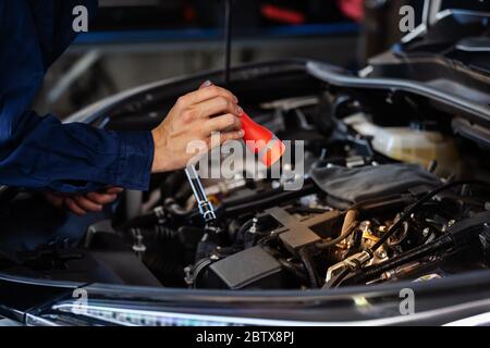 un mécanicien de sexe masculin tient et brille la lampe de poche pour vérifier un problème de moteur de voiture Banque D'Images