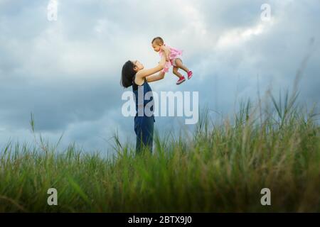 Famille heureuse ensemble, parents avec leur bébé au coucher du soleil. Mère élevant bébé dans l'air - effet de couleur vibrant Banque D'Images