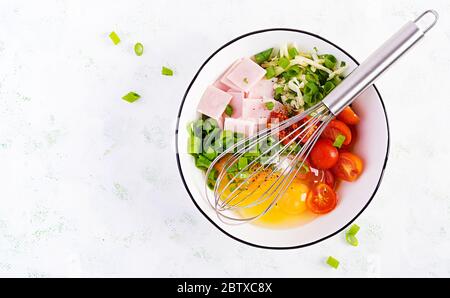 Ingrédients des omelettes : œufs, jambon, tomates, herbes vertes, lait et fromage sur la table lumineuse. Vue de dessus, au-dessus, à plat Banque D'Images