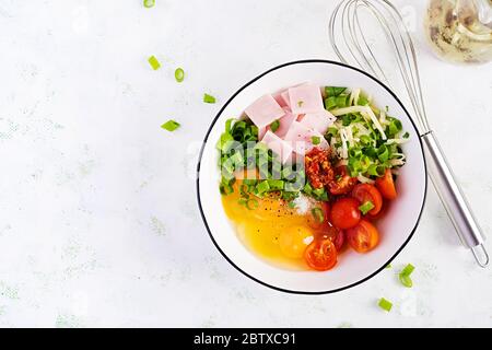 Ingrédients des omelettes : œufs, jambon, tomates, herbes vertes, lait et fromage sur la table lumineuse. Vue de dessus, au-dessus, à plat Banque D'Images