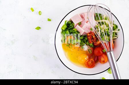 Ingrédients des omelettes : œufs, jambon, tomates, herbes vertes, lait et fromage sur la table lumineuse. Vue de dessus, au-dessus, à plat Banque D'Images