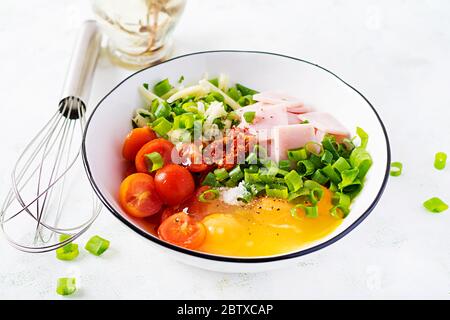 Ingrédients des omelettes : œufs, jambon, tomates, herbes vertes, lait et fromage sur la table lumineuse. Banque D'Images