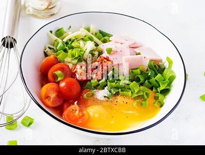 Ingrédients des omelettes : œufs, jambon, tomates, herbes vertes, lait et fromage sur la table lumineuse. Banque D'Images