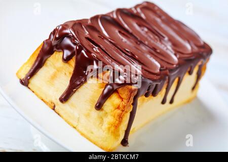 Gros plan sur le cheesecake traditionnel rectangulaire lviv de fromage cottage ukrainien avec raisins secs et glaçage au chocolat noir servi sur un c blanc Banque D'Images