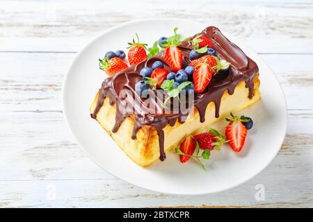 Cheesecake ukrainien occidental cuit au four de fromage cottage avec glaçage au chocolat noir sur le dessus avec des bleuets frais, des fraises, des feuilles de menthe sur un c blanc Banque D'Images