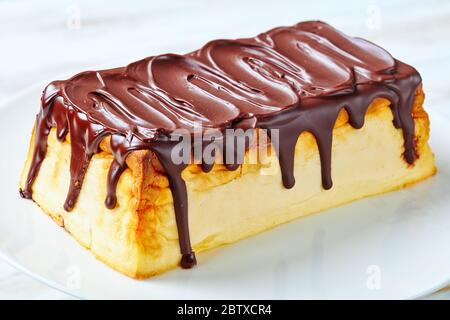 Cheesecake de fromage cottage ukrainien avec raisins secs et glaçage au chocolat noir servi sur une assiette blanche sur fond de bois blanc, gros plan Banque D'Images