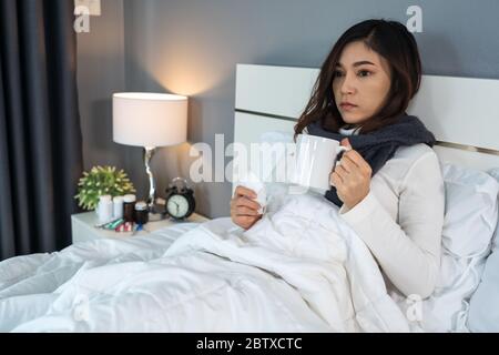 femme malade buvant une tasse d'eau chaude sur un lit Banque D'Images