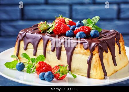 Cuisine d'Europe de l'est : cheesecake au fromage cottage avec glaçage au chocolat noir sur le dessus, bleuets frais, fraises, feuilles de menthe sur un gâteau blanc Banque D'Images