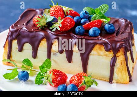 Syrnyk Lviv rectangulaire ukrainien ou cheesecake Lviv de fromage cottage, raisins secs avec glaçage au chocolat servis avec des bleuets frais, des fraises, de la menthe Banque D'Images