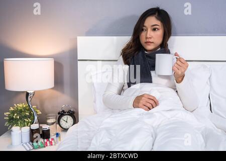 femme malade buvant une tasse d'eau chaude sur un lit Banque D'Images