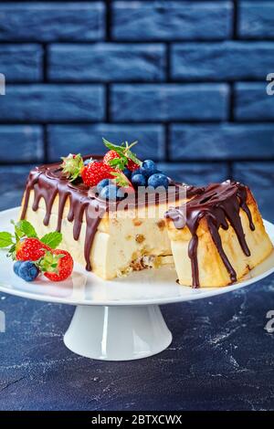 Authentique cheesecake ukrainien au fromage fermier avec garniture chocolat noir et myrtilles fraîches, fraises, sur fond de béton foncé devant Banque D'Images