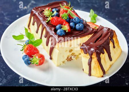 Cheesecake au fromage cottage avec glaçage au chocolat noir sur le dessus, bleuets frais, fraises, feuilles de menthe sur un gâteau blanc stand sur un dos en béton foncé Banque D'Images