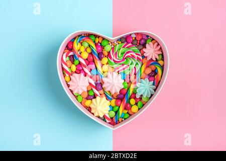 Mélanger les bonbons au chocolat colorés se trouvent dans une boîte cadeau en forme de coeur sur fond coloré Flat Lay vue du dessus Banque D'Images