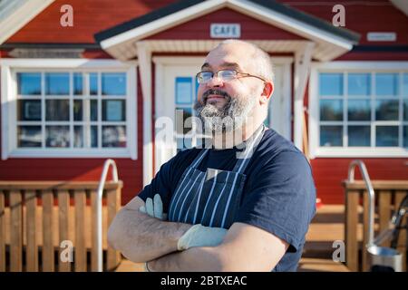 Portrait d'un homme mûr confiant avec barbe, employé du restaurant portant des tabliers debout devant le restaurant. Concept de petite entreprise. Banque D'Images