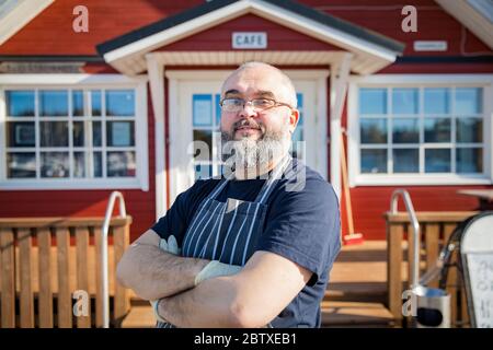 Portrait d'un homme mûr confiant avec barbe, employé du restaurant portant des tabliers debout devant le restaurant. Concept de petite entreprise. Banque D'Images