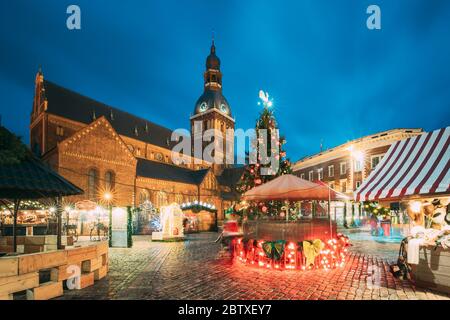 Riga, Lettonie. Marché de Noël sur la place du Dôme avec la cathédrale du Dôme de Riga. Arbre de Noël et maisons de commerce. Célèbre site d'intérêt à la soirée d'hiver à Banque D'Images