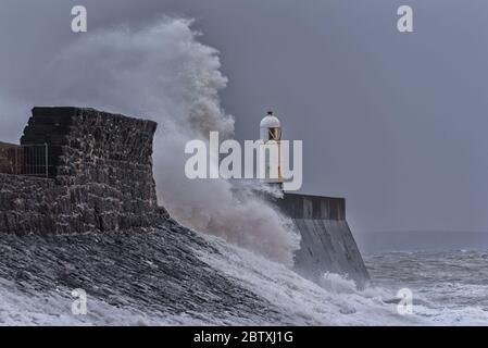 D'énormes vagues se brisent contre une jetée en pierre, avec un phare unique à la fin, pendant une tempête hivernale majeure. L'emplacement est Porthcawl, pays de Galles Banque D'Images