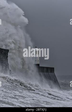 D'énormes vagues se brisent contre une jetée en pierre, avec un phare unique à la fin, pendant une tempête hivernale majeure. L'emplacement est Porthcawl, pays de Galles Banque D'Images