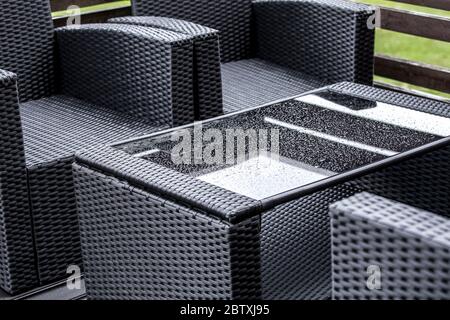 Vue rapprochée de meubles de jardin en rotin et en verre en plastique synthétique humide. Concept d'entretien des meubles de jardin. Banque D'Images