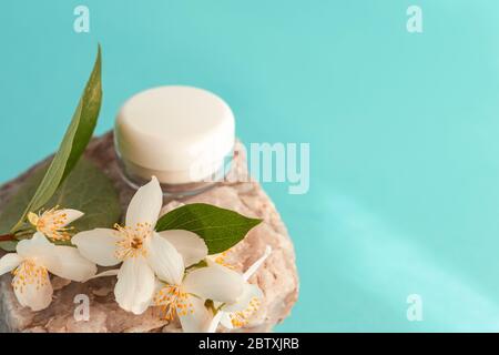 Pot de crème cosmétique en blanc blanc blanc emballage blanc sur la pierre avec fleur de jasmin, fond bleu, espace de copie. Mise au point sélective Banque D'Images
