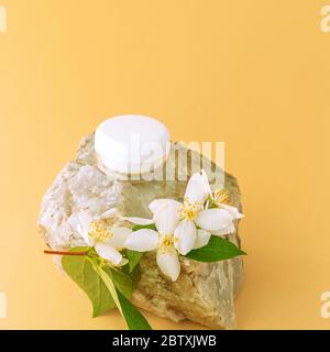 Pot de crème cosmétique en blanc blanc blanc emballage blanc sur la pierre avec fleur de jasmin, fond jaune, espace de copie. Banque D'Images