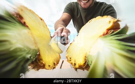 Jeune homme souriant coupant l'ananas - gros plan main mâle tenant un couteau tranchant préparant des fruits frais tropicaux Banque D'Images