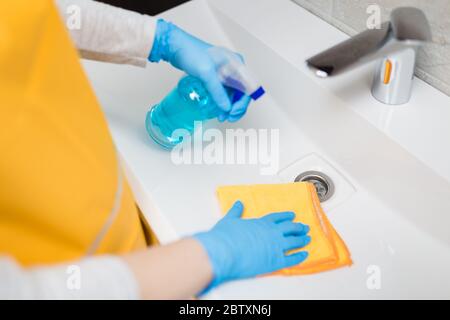Gros plan des mains de femme dans des gants de protection nettoyage et polissage de l'évier de salle de bains avec un chiffon et un vaporisateur d'assainisseur. Concept d'hygiène. Banque D'Images